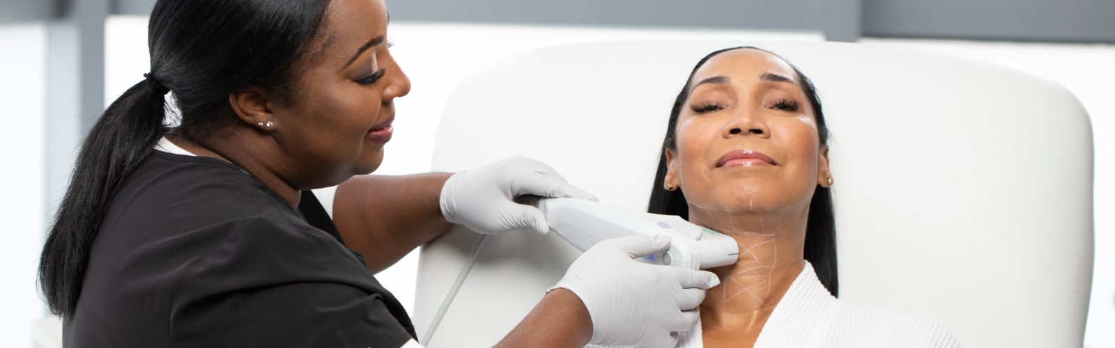 A woman in black scrubs performing Ultherapy on the neck region of a female.