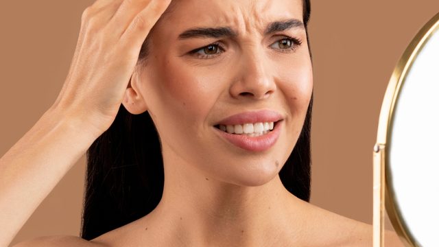 Woman holding her hand on the side of her head while staring into a mirror.