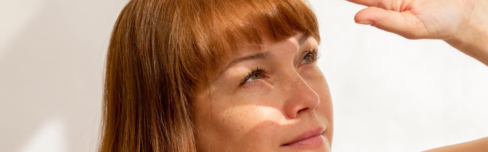 Woman with red hair using her left hand to block the sunlight from her eyes.