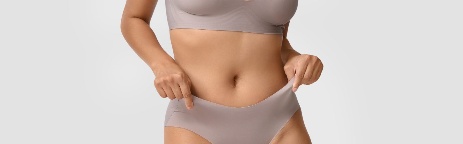 Closeup of woman's stomach area wearing light colored bra and underwear.