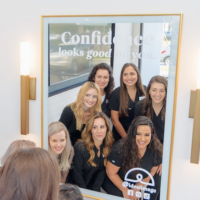 Group of woman smiling at their reflection in a mirror.