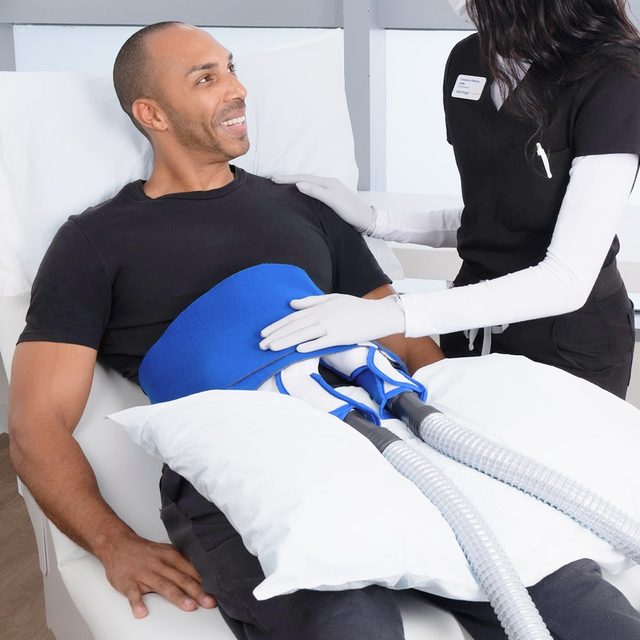 Adult male wearing black clothing receiving Cooltone in the abdomen, being administered by a provider in dark clothes wearing a nametag.