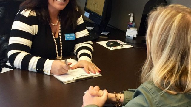 Two women sitting at a desk speaking with each other.