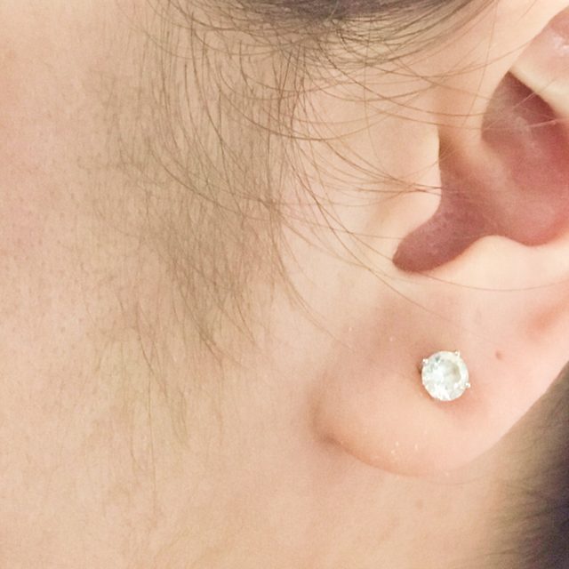 Side angle of a woman's white earring and black hair.
