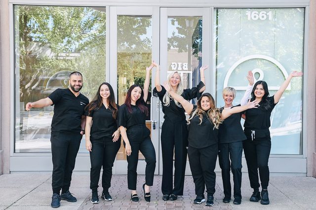 Seven people wearing black clothing smiling in front of a building.