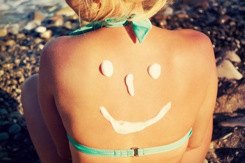A woman with sunscreen on her back with the shape of a smile.