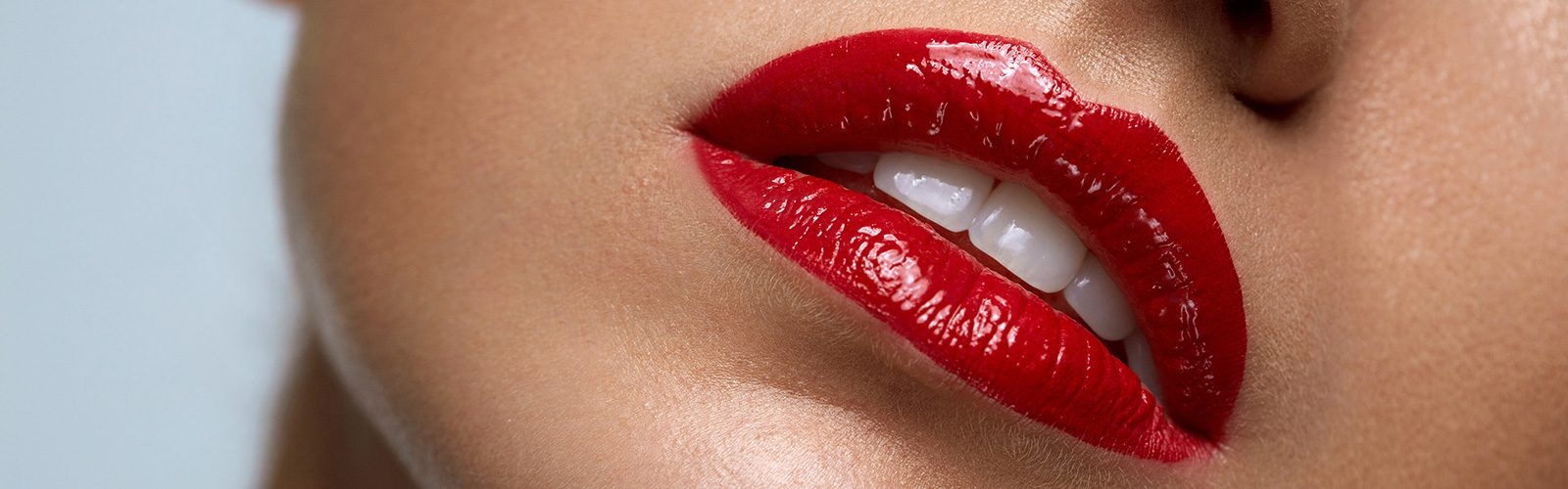 Closeup on a person's mouth and teeth with bright red lipstick.