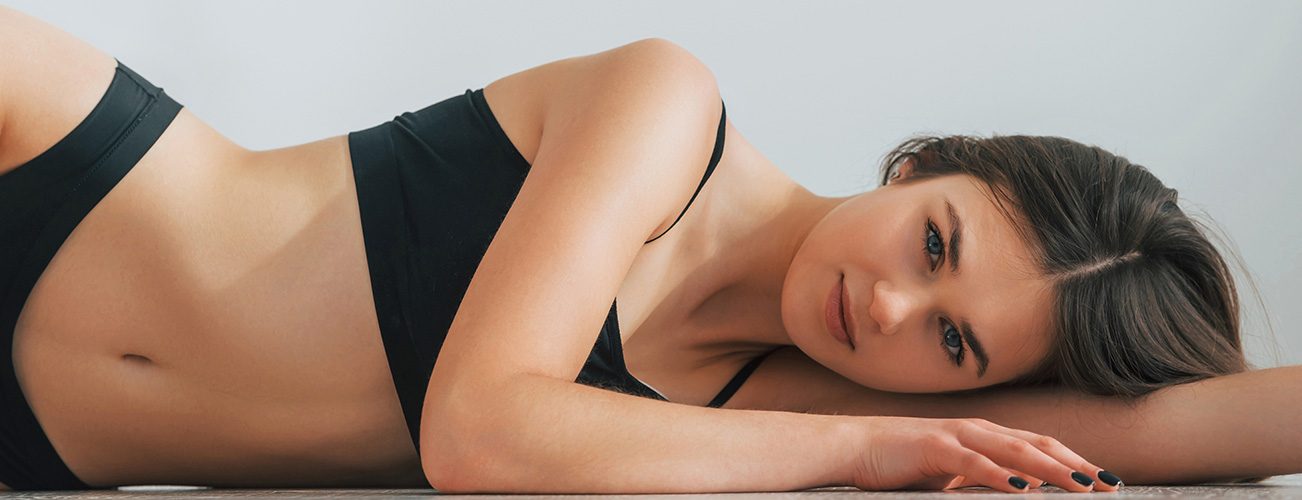 Woman with dark hair lying down wearing a black bra and underwear.