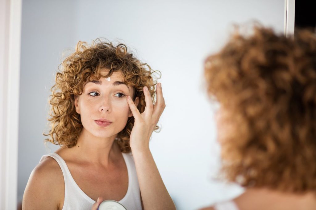 Woman with curly hair applying skincare to face.