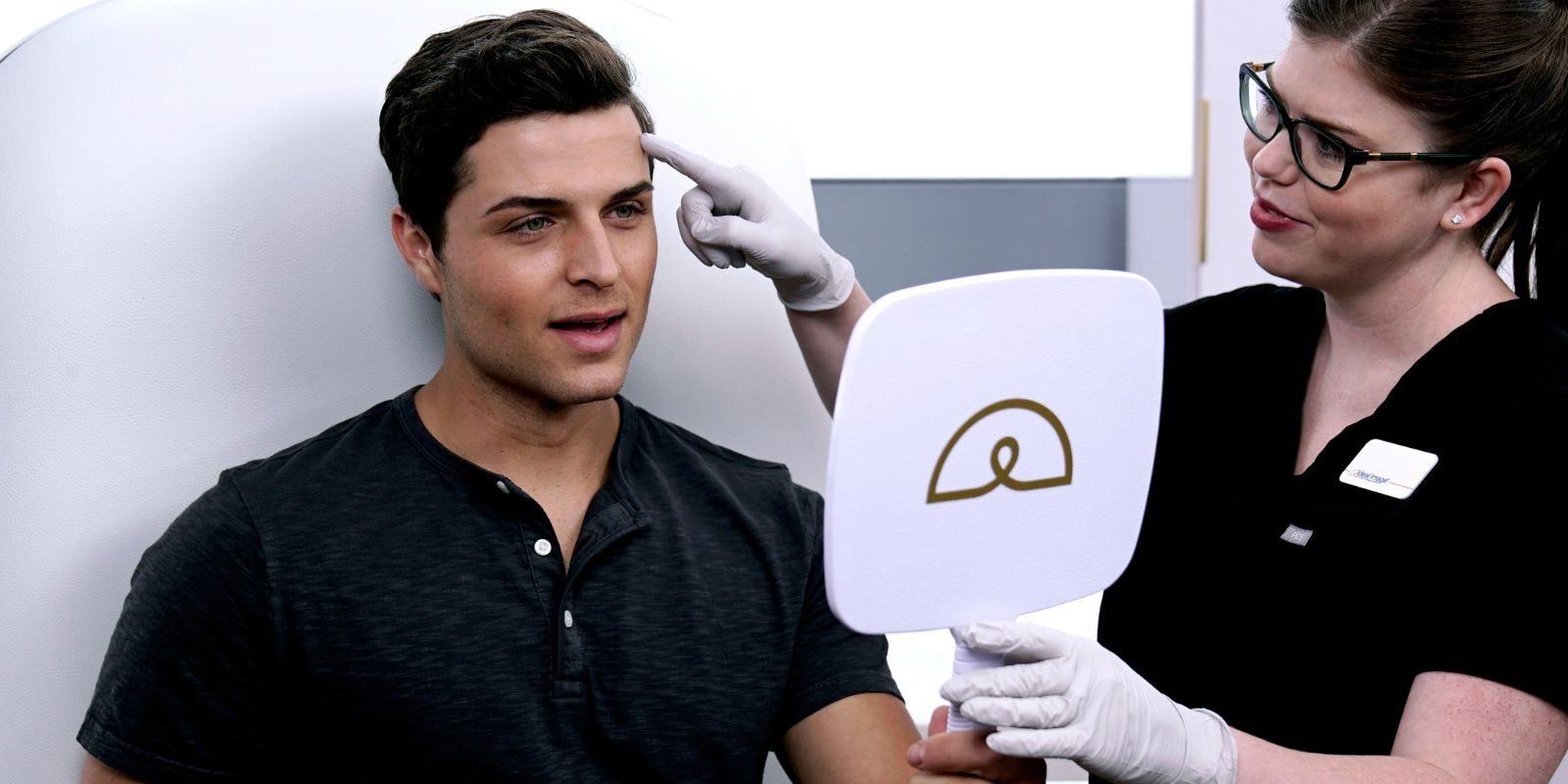 man looking into mirror being held by a medical technician
