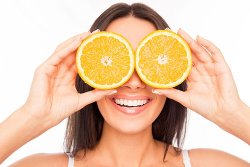 woman holding orange slices to eyes