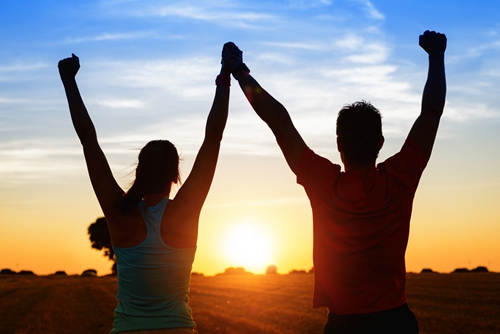 silhouette of young woman and man with arms raised at sunset