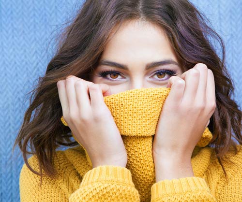young woman pulling sweater up over face