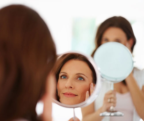 woman looking in mirror - touching face