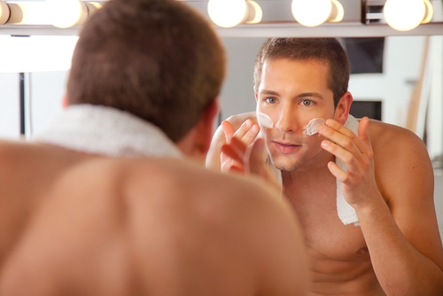 young man applying cream to face, looking in mirror